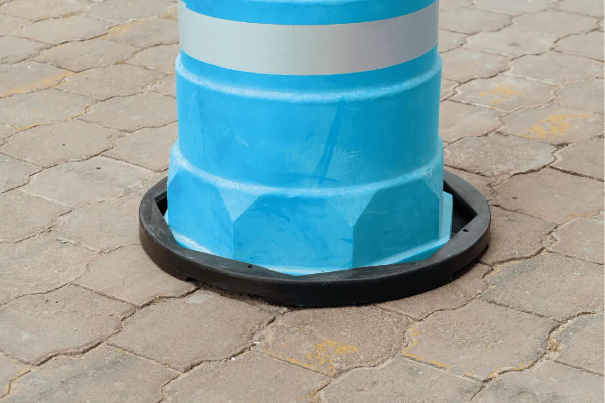 Trafitambo azul claro con banda reflejante sobre su base negra redonda en un piso de adoquín