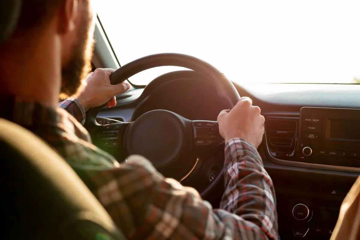 Conductor con camisa a cuadros con las dos manos en el volante durante un viaje