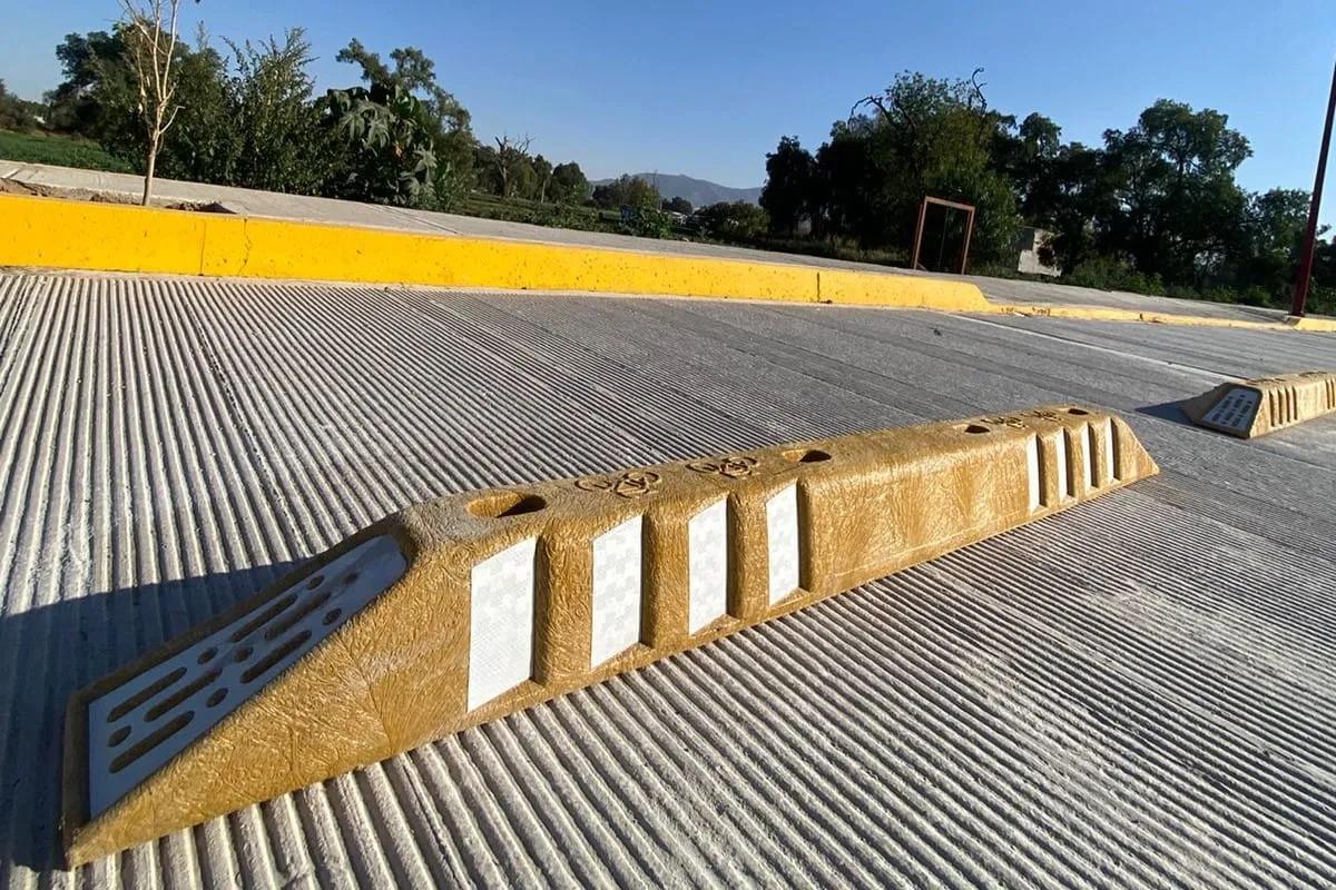 Canalizador vial amarillo con reflejantes blancos anclado sobre concreto estriado, con otro canalizador al fondo