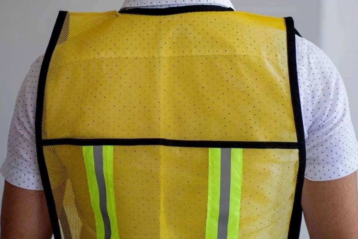 Espalda de una persona con chaleco de malla amarillo y dos franjas reflejantes verticales