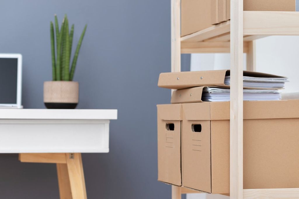 Dos cajas tipo archivo de cartón kraft con asas troqueladas en un anaquel, con carpetas de palanca encima