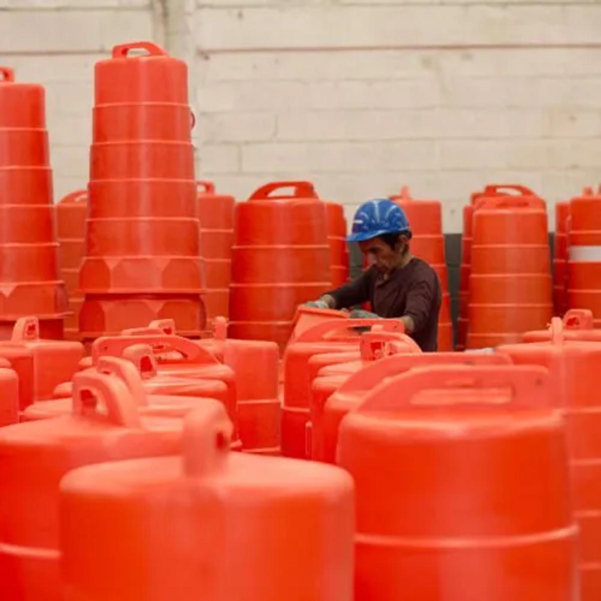 Trabajador con casco azul entre decenas de trafitambos naranjas con asa dentro de una nave industrial