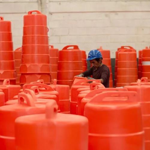 Trabajador con casco azul entre decenas de trafitambos naranjas con asa dentro de una nave industrial