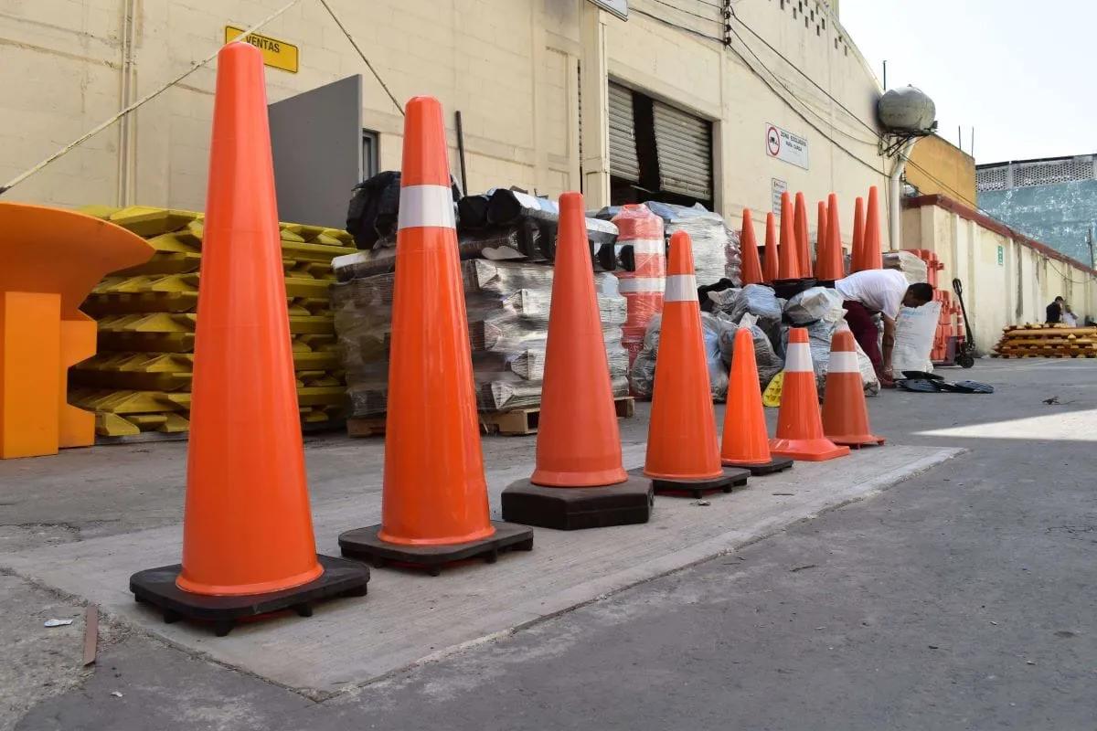 Conos viales naranja formados en un patio de almacén con trafitambos y topes empacados al fondo