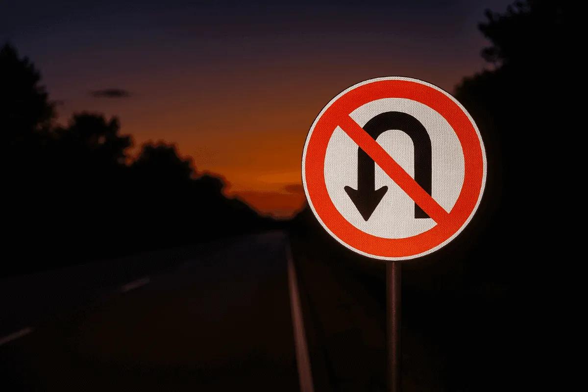 Señal de prohibido dar vuelta en U junto a una carretera al atardecer