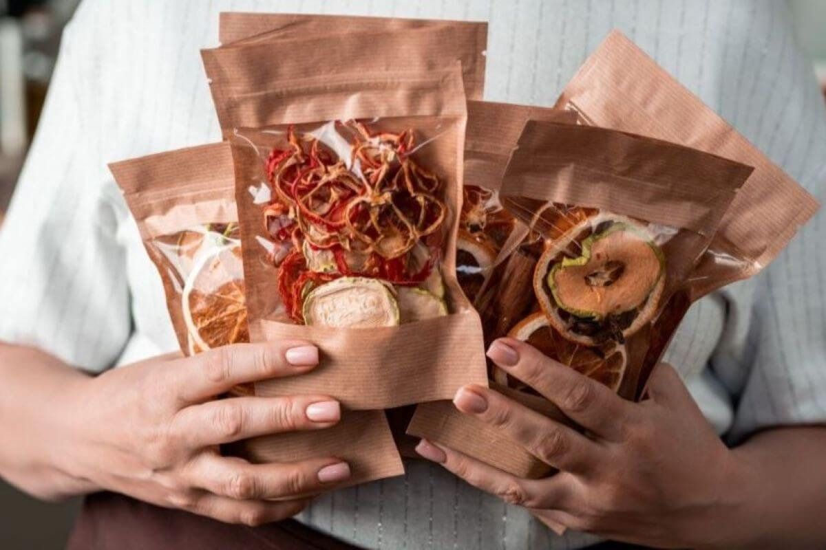 Manos sostienen bolsas de papel kraft con ventana transparente llenas de fruta deshidratada