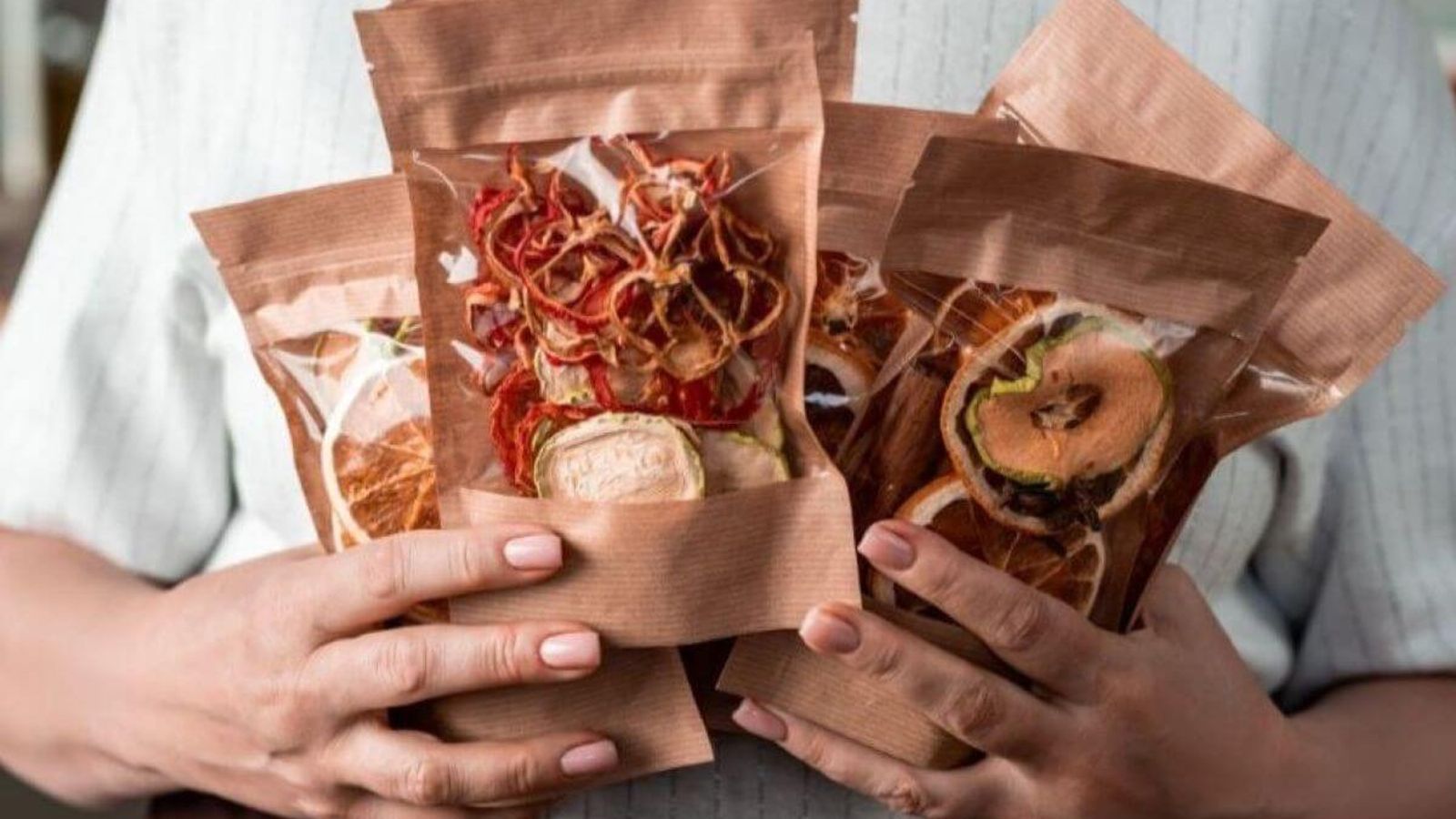 Manos sostienen bolsas de papel kraft con ventana transparente llenas de fruta deshidratada