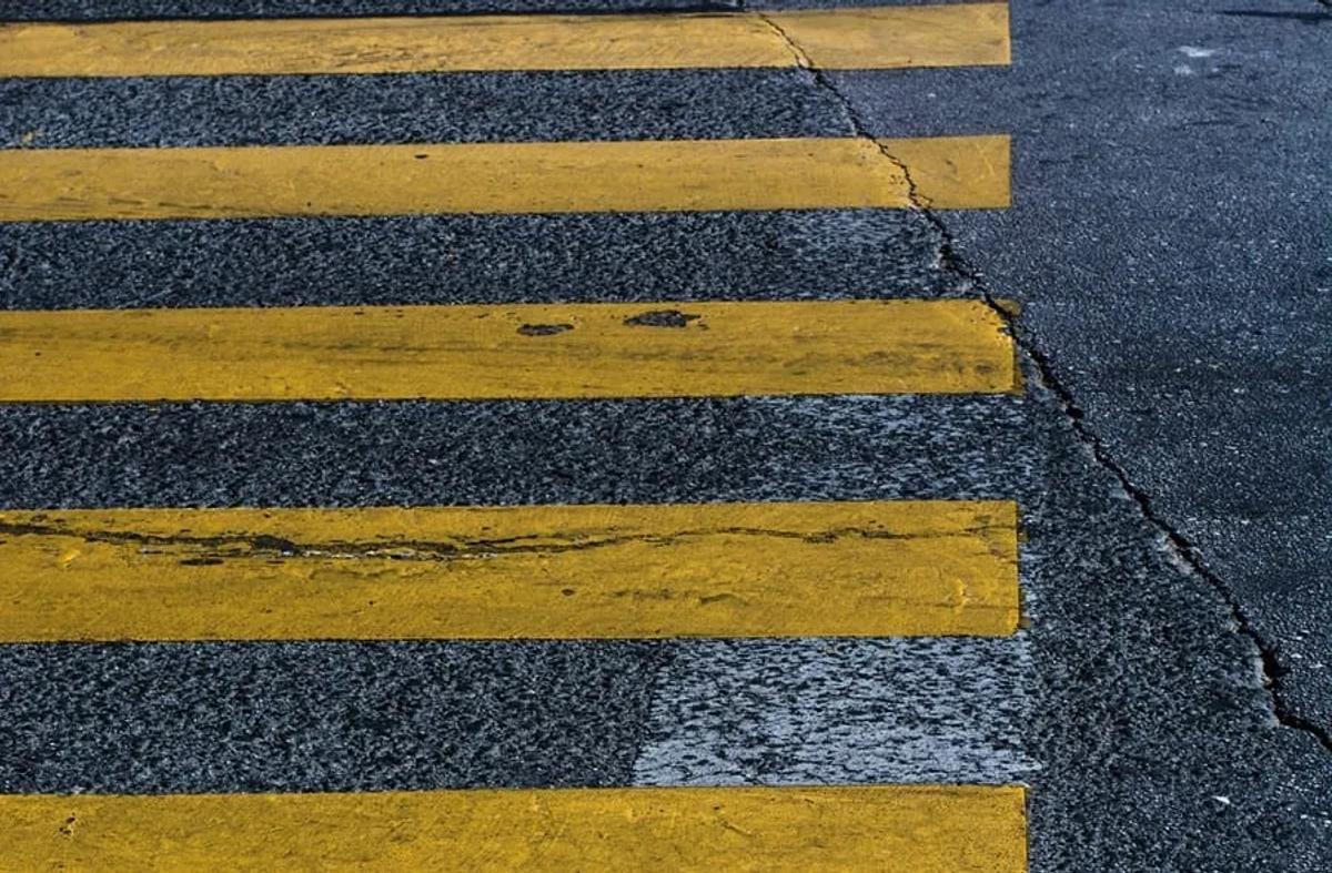 Franjas amarillas desgastadas de un paso peatonal pintadas sobre asfalto oscuro con una grieta