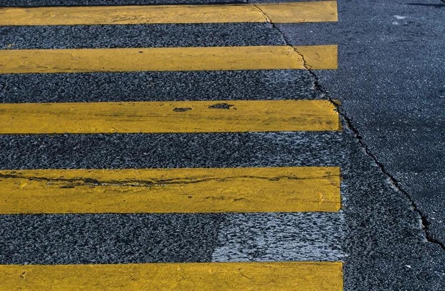 Franjas amarillas desgastadas de un paso peatonal pintadas sobre asfalto oscuro con una grieta