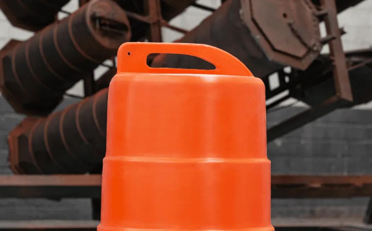 Parte superior de un trafitambo naranja con asa integrada, frente a estructuras metálicas oxidadas