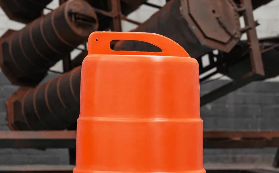 Parte superior de un trafitambo naranja con asa integrada, frente a estructuras metálicas oxidadas