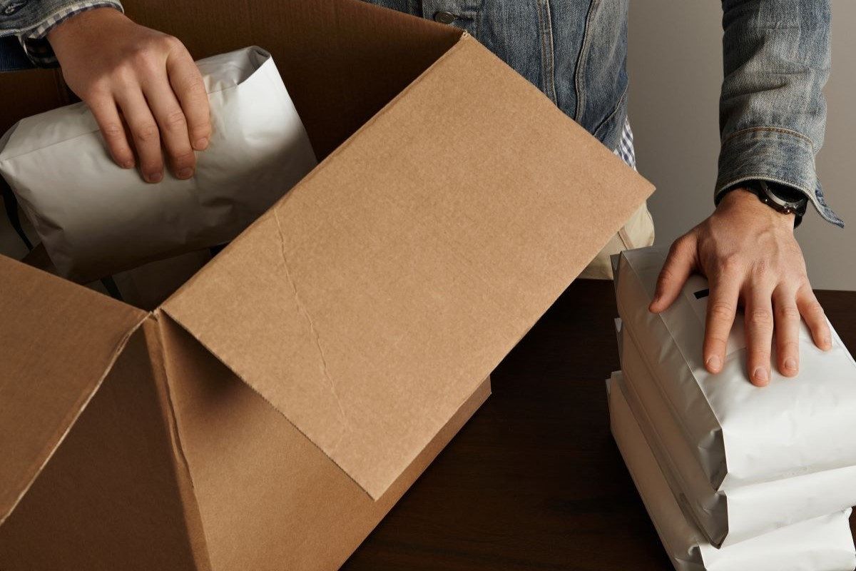 Manos acomodan bolsas de envío blancas dentro de una caja de cartón abierta sobre un escritorio