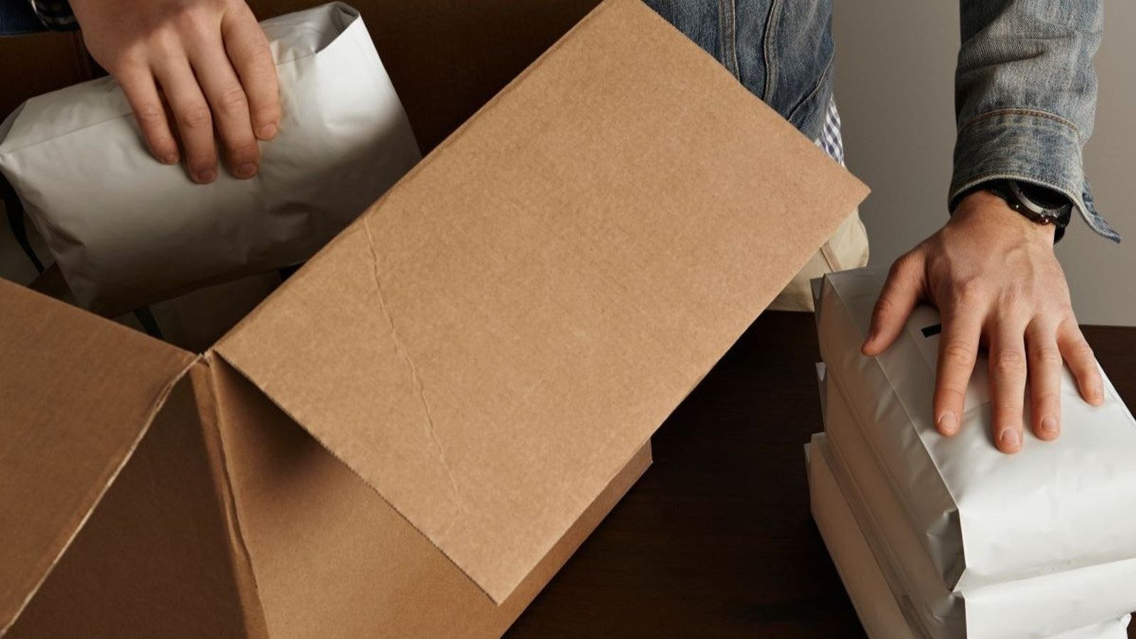 Manos acomodan bolsas de envío blancas dentro de una caja de cartón abierta sobre un escritorio
