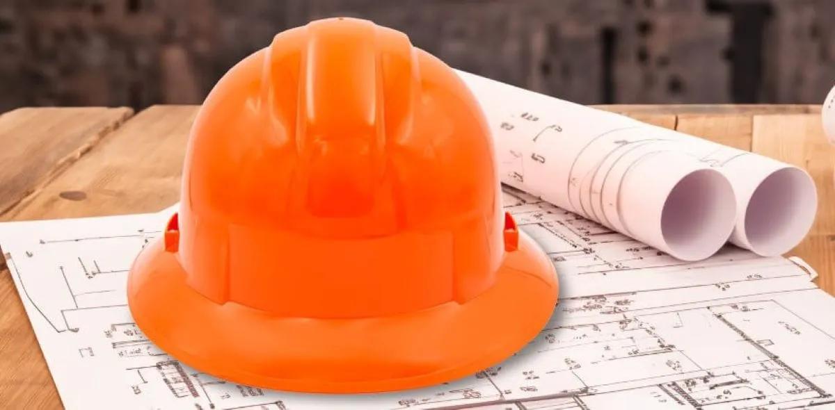 Casco de seguridad naranja de ala completa sobre planos de construcción en una mesa de madera