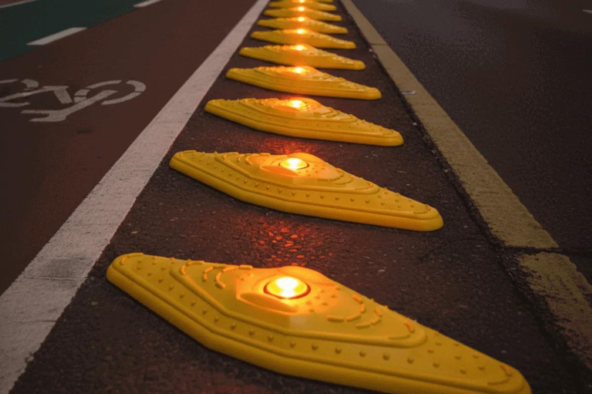 Canalizadores Kayak amarillos con luces ámbar encendidas separan una ciclovía roja del carril vehicular al anochecer