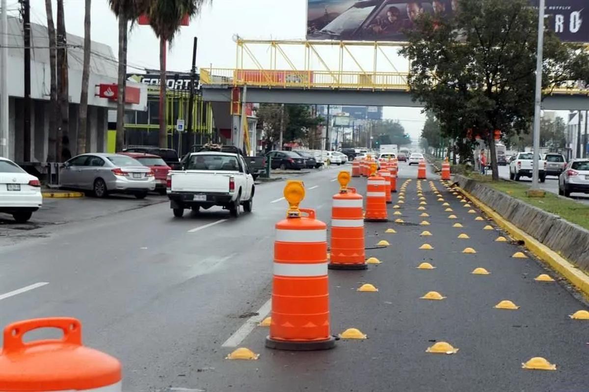 Fila de trafitambos naranjas con lámparas de destello y botones viales amarillos separando un carril en una avenida