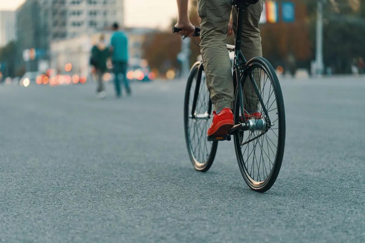 Ciclista con tenis rojos y pantalón caqui pedalea una bicicleta negra por una calle amplia
