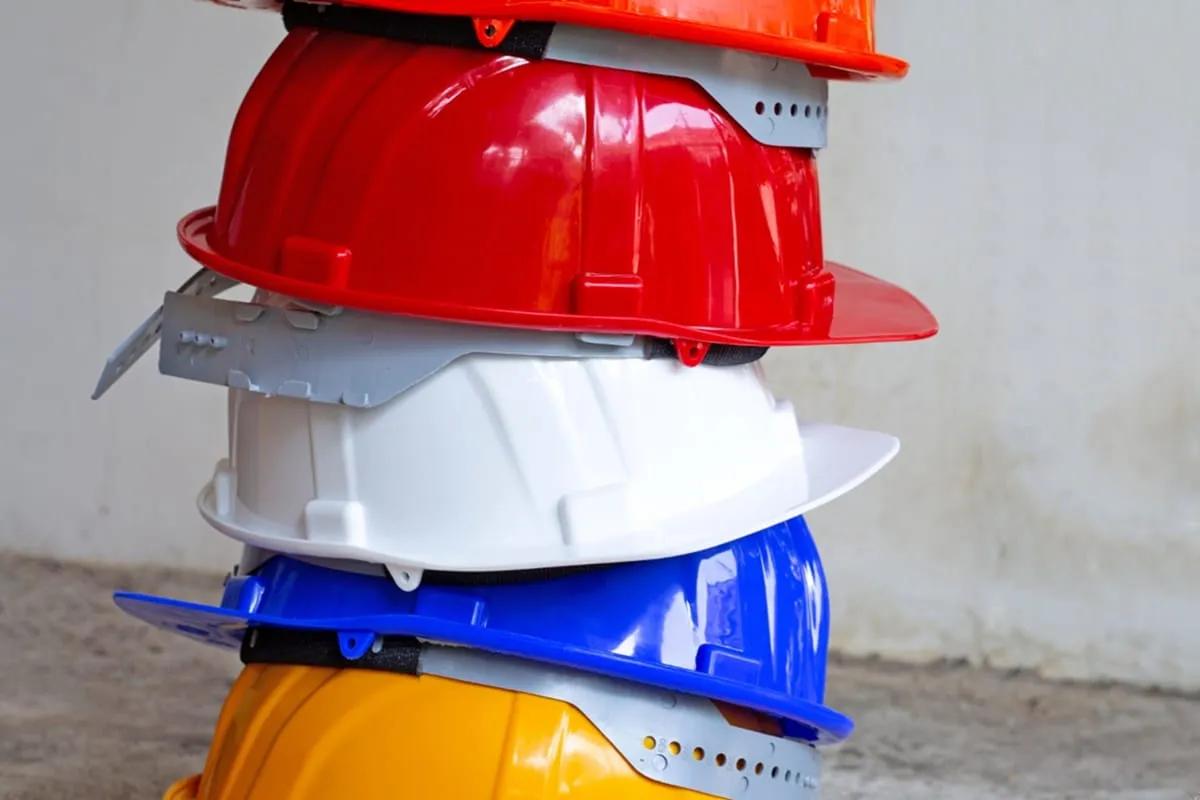 Cascos de seguridad apilados en naranja, rojo, blanco, azul y amarillo contra un muro de concreto