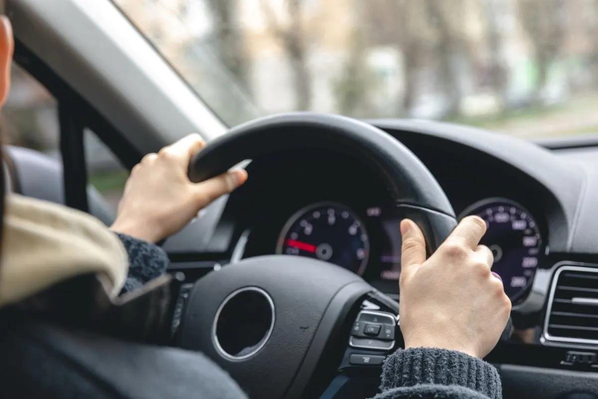 Manos de un conductor sobre el volante de un auto con el tablero y el velocímetro al frente