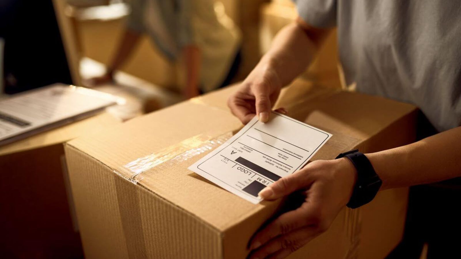 Persona coloca una etiqueta de envío sobre una caja de cartón cerrada con cinta transparente