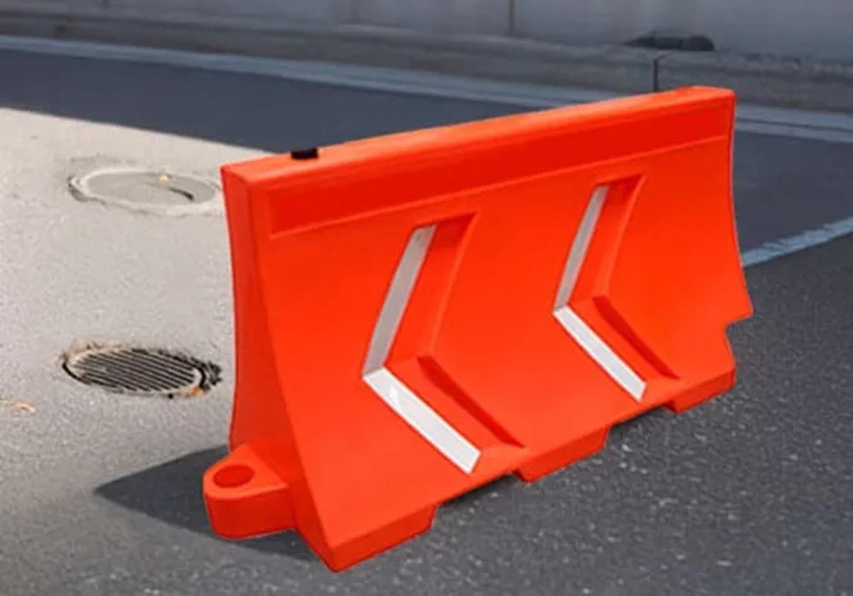 Barrera de plástico naranja con dos flechas reflejantes junto a una alcantarilla en una calle