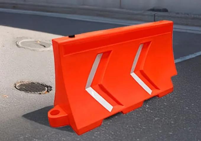 Barrera de plástico naranja con dos flechas reflejantes junto a una alcantarilla en una calle