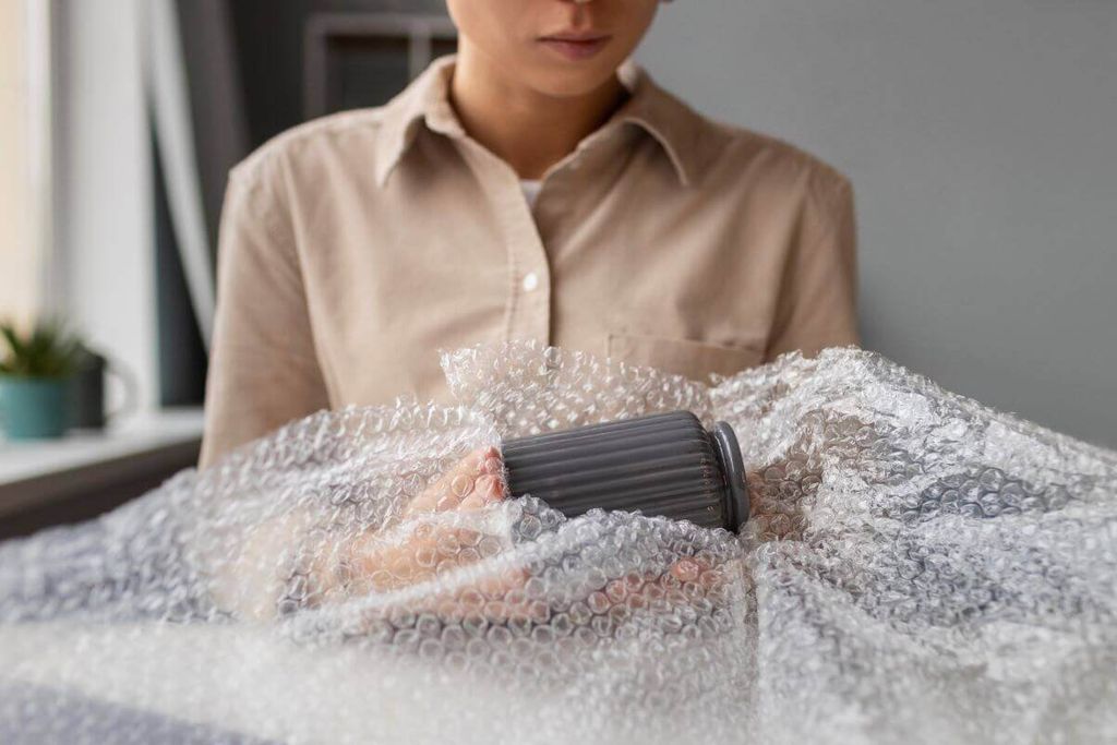 Persona envuelve un vaso gris con plástico de burbujas sobre una mesa