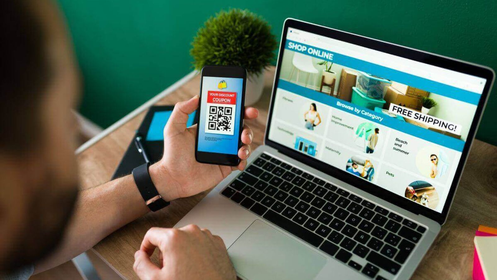 Hombre sostiene un celular con un cupón QR frente a una laptop que muestra una tienda en línea