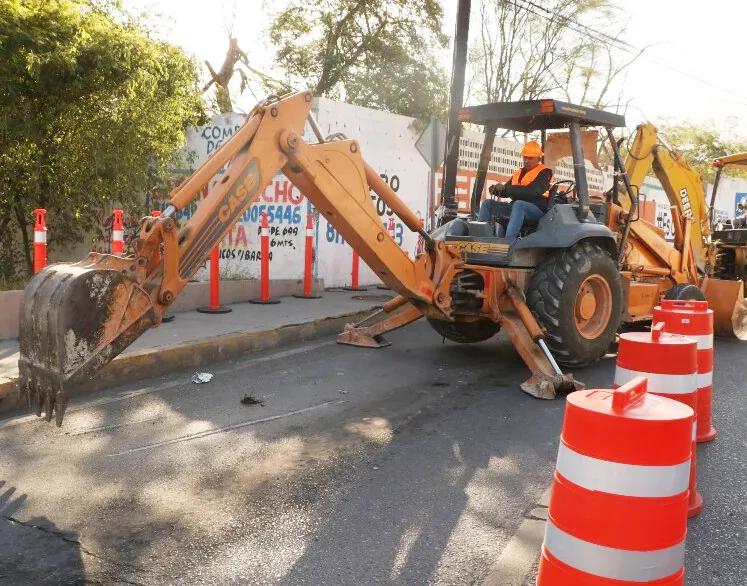 Retroexcavadora trabajando en una calle con trafitambos naranja con bandas blancas al frente y canalizadores en la banqueta