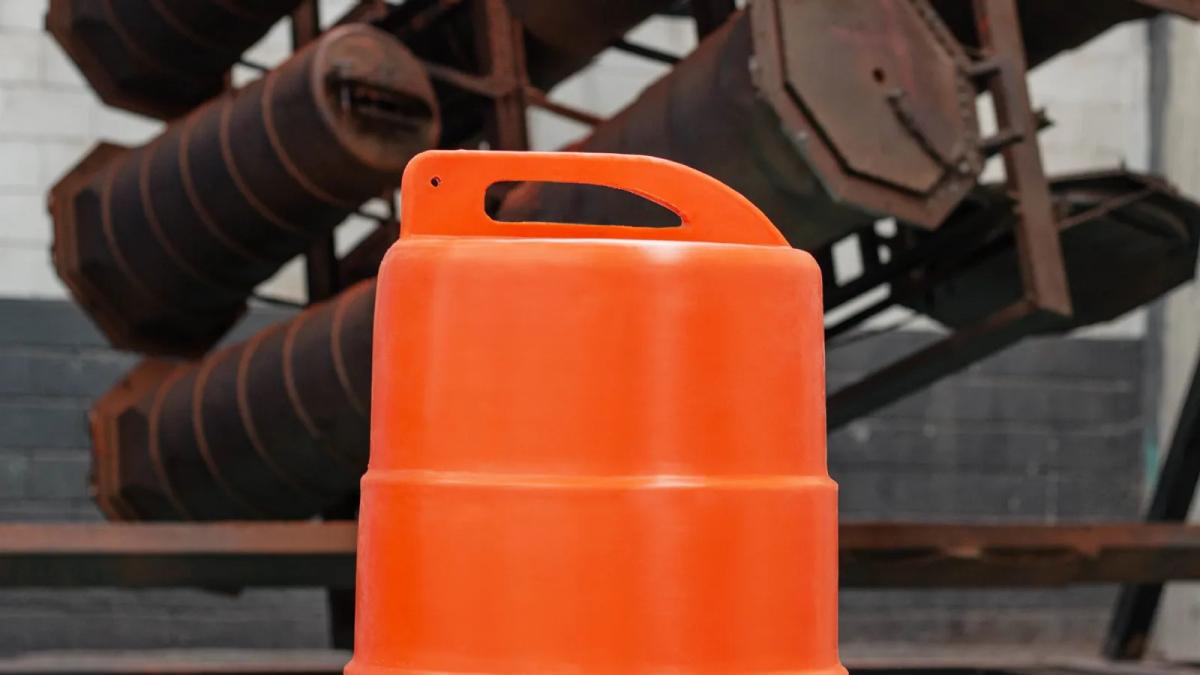 Parte superior de un trafitambo naranja con asa integrada, frente a maquinaria industrial oxidada