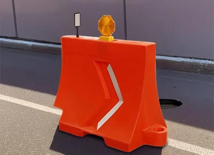 Barrera de plástico naranja con flecha reflejante, lámpara de destello y delineador sobre una vialidad