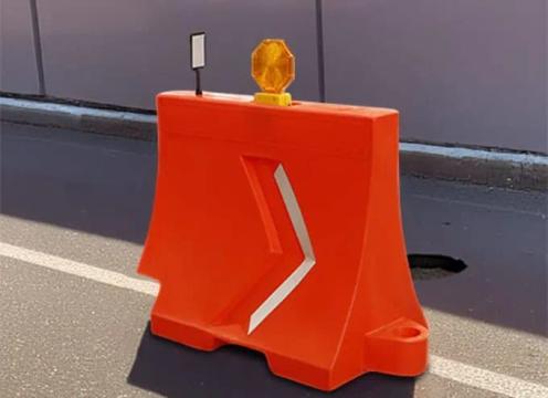 Barrera de plástico naranja con flecha reflejante, lámpara de destello y delineador sobre una vialidad