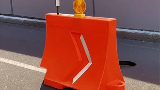 Barrera de plástico naranja con flecha reflejante, lámpara de destello y delineador sobre una vialidad