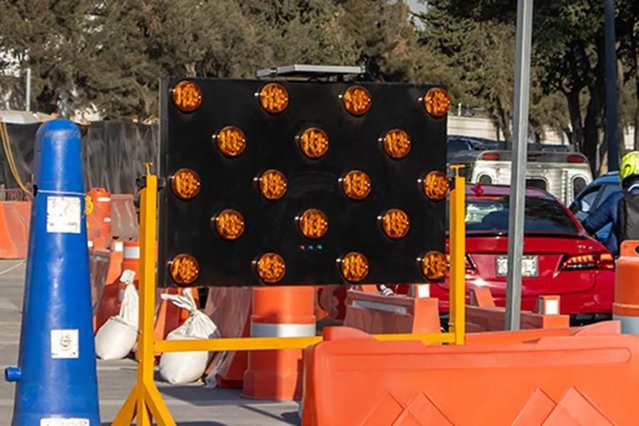 Flechero luminoso de luces ámbar sobre soporte amarillo en una obra vial de la Ciudad de México, junto a un cono azul