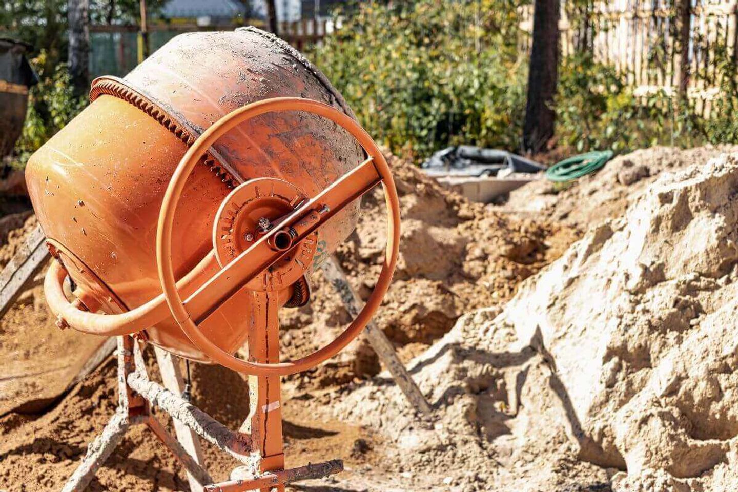 Mezcladora de concreto color naranja en una obra con zanja excavada al fondo