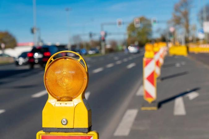 Lámpara de destello ámbar sobre una barrera en una avenida con obra marcada por balizas rojas y blancas