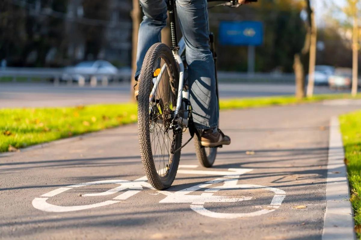 Ciclista en bicicleta de montaña sobre una bicisenda gris con el símbolo de bici pintado, entre áreas de pasto