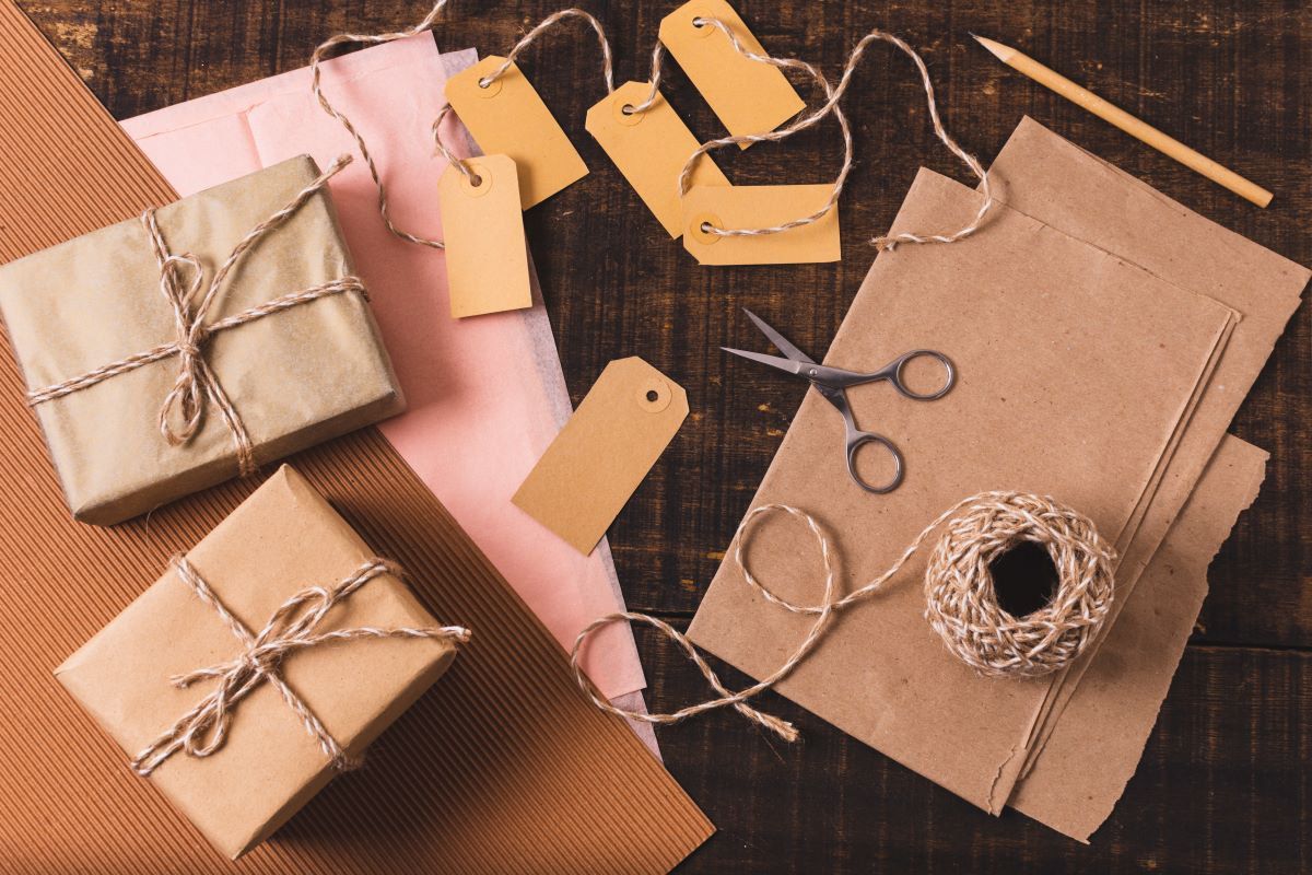 Paquetes envueltos en papel kraft con cordón de yute, etiquetas colgantes, tijeras y lápiz sobre una mesa de madera