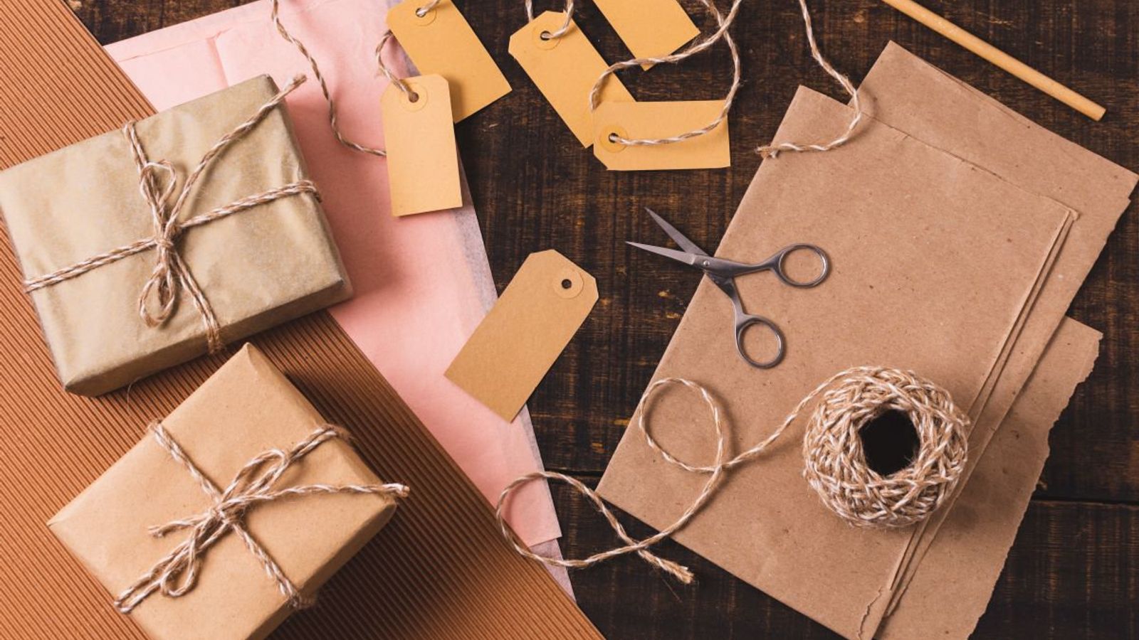 Paquetes envueltos en papel kraft con cordón de yute, etiquetas colgantes, tijeras y lápiz sobre una mesa de madera