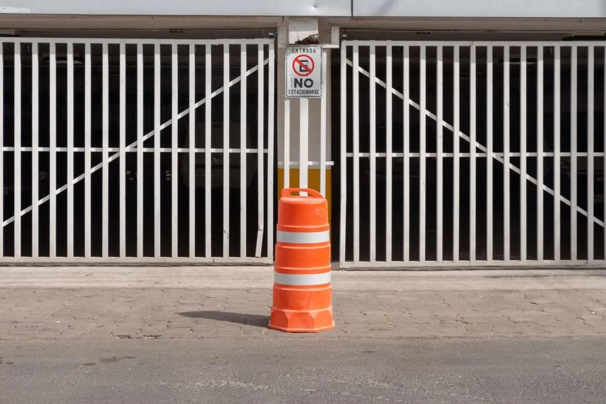 Trafitambo naranja con dos bandas reflejantes frente a un portón con letrero de no estacionarse