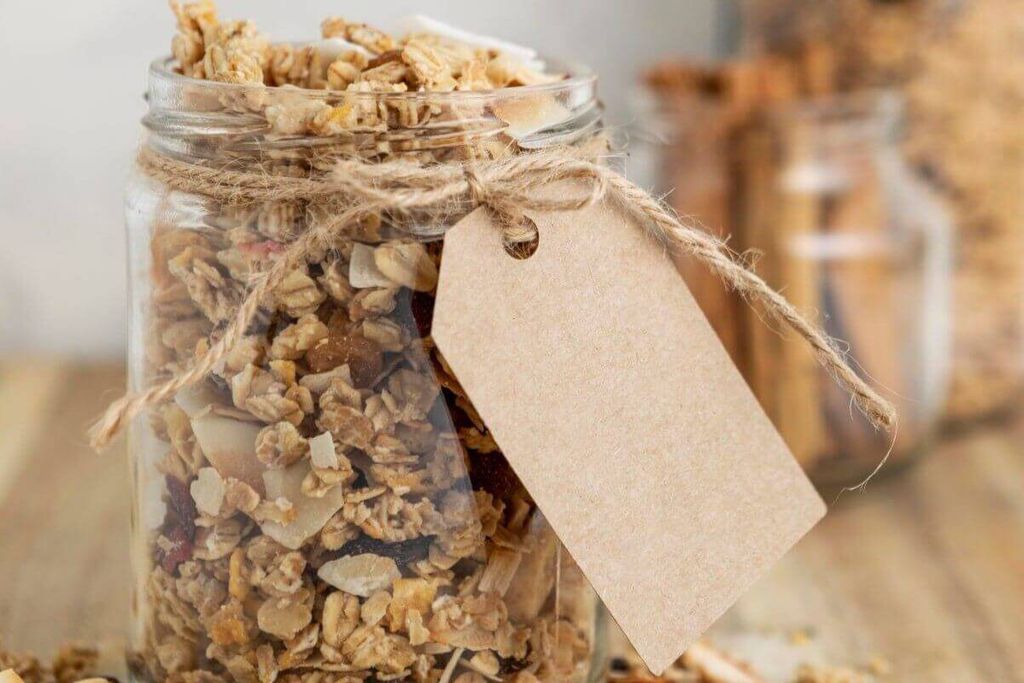 Frasco de vidrio con granola atado con hilo de yute y una etiqueta de cartón kraft en blanco