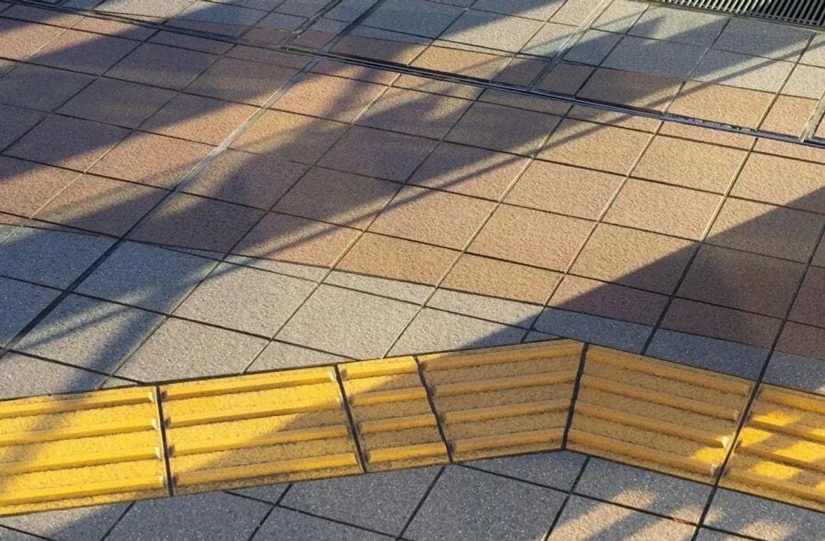 Losetas podotáctiles amarillas de barras guía que forman una ruta en zigzag sobre una banqueta de baldosas beige