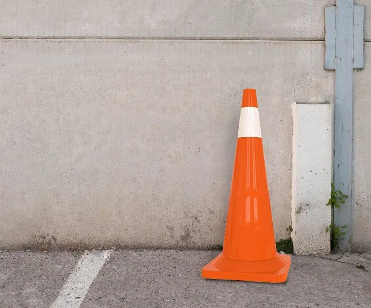 Cono vial naranja con franja reflejante blanca junto a un muro de concreto