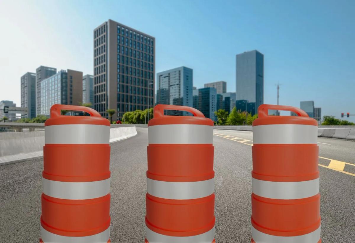 Tres trafitambos naranjas con bandas reflejantes blancas sobre una vialidad elevada, con edificios altos al fondo