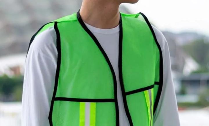 Persona con chaleco de seguridad verde neón de malla con ribete negro y franjas reflejantes