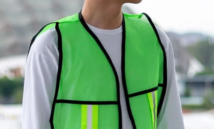 Persona con chaleco de malla verde fluorescente con ribete negro y franjas reflejantes sobre camisa blanca