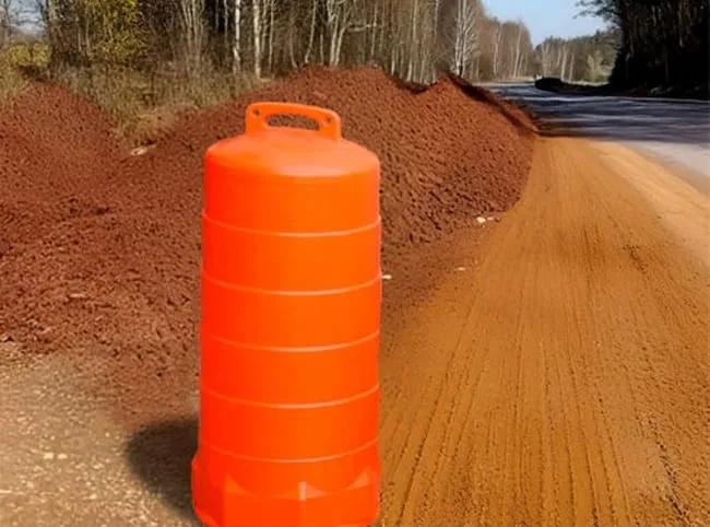 Trafitambo naranja sin reflejantes junto a montículos de tierra en un camino en obra
