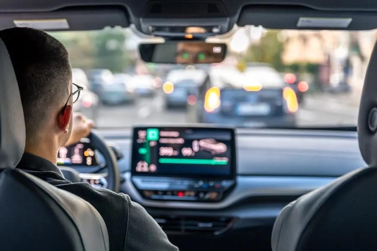 Conductor con lentes al volante de un auto con pantalla digital en el tablero, en tráfico urbano