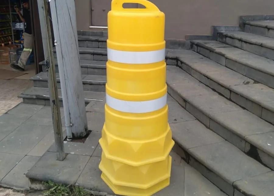 Trafitambo amarillo con dos bandas reflejantes blancas junto a unas escaleras de piedra en una banqueta