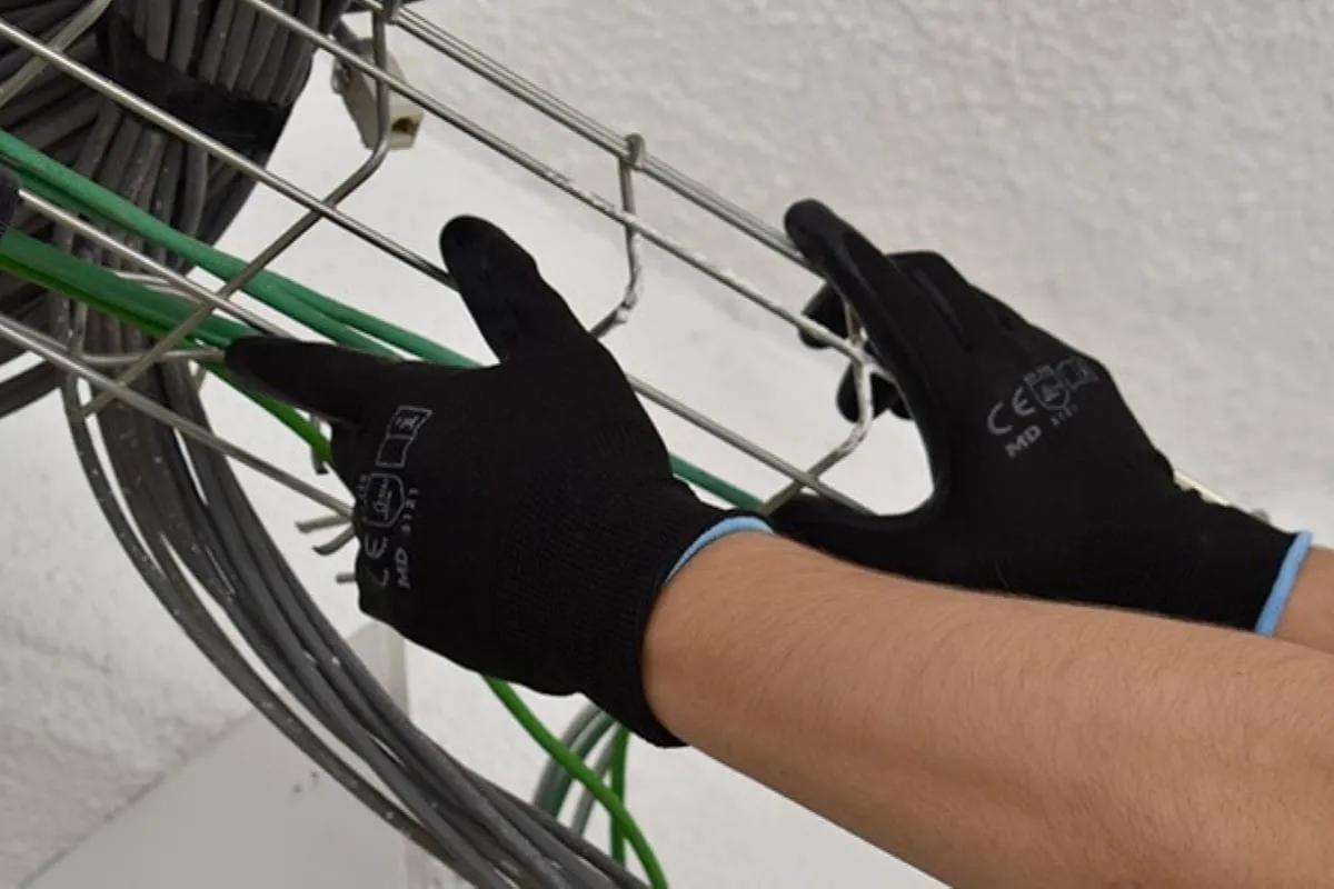 Manos con guantes negros tejidos acomodan cables verdes y grises en una charola de alambre